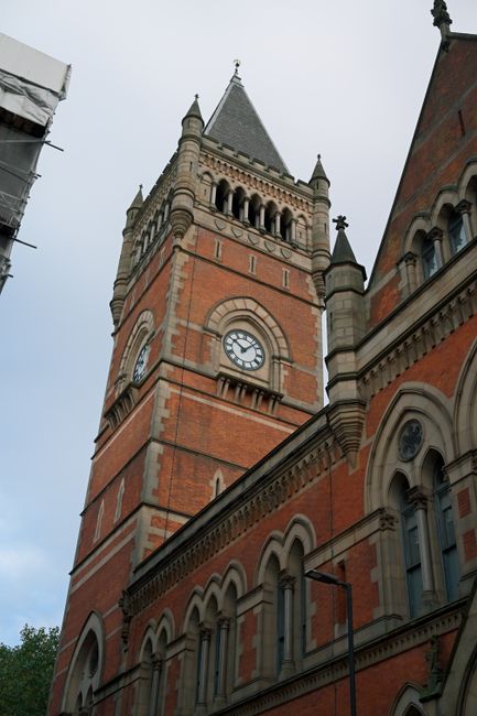A black and white photograph of a historic clock tower featuring a rounded, domed roof topped with a weather vane, located in an urban setting. The tower's clock faces are visible, showing the time as